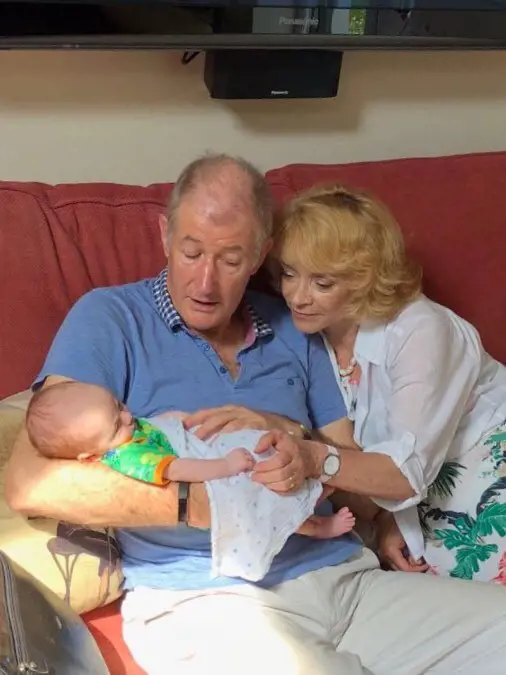 Sue and her spouse holding their grandchild in their arms in 28 May 2018